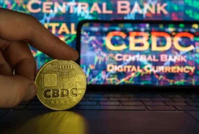 A hand holding a gold coin with the word 'CBDC' inscribed on it