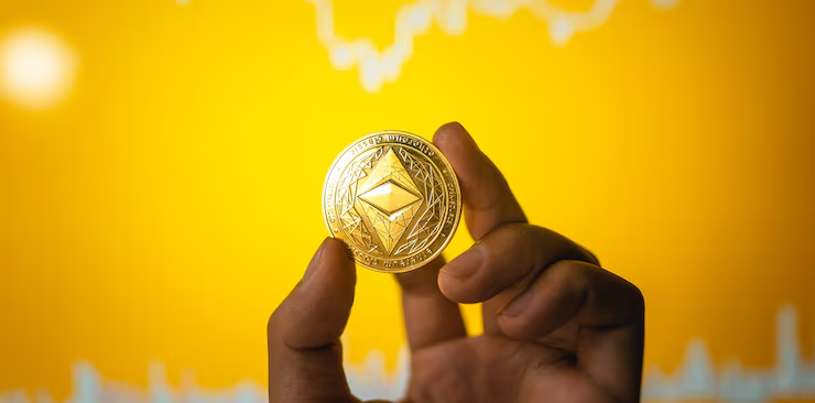 ETH crypto coin in the hand in front of the desk and on the computer graph.
