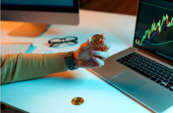 crypto is a scam; a man holding a gold bitcoin in front of a laptop 
