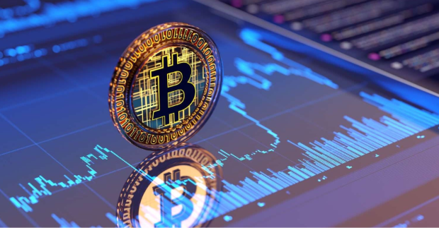 Bitcoin coin standing upright on a digital trading screen displaying blue price charts and volume bars.