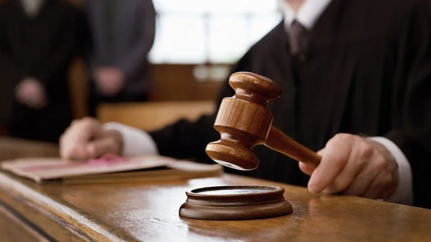 A judge holding a wooden gavel over its base in a courtroom, with legal documents on the table.