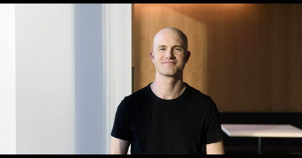 Image of Brian Armstrong wearing a black shirt with a white and wood background