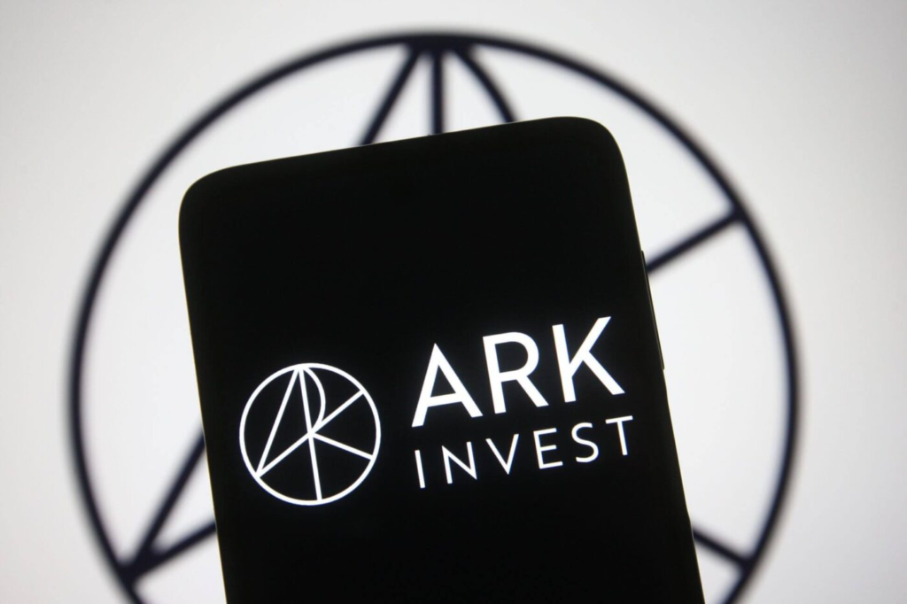 ARK Invest logo displayed on a smartphone screen against a blurred background featuring the company's circular emblem.