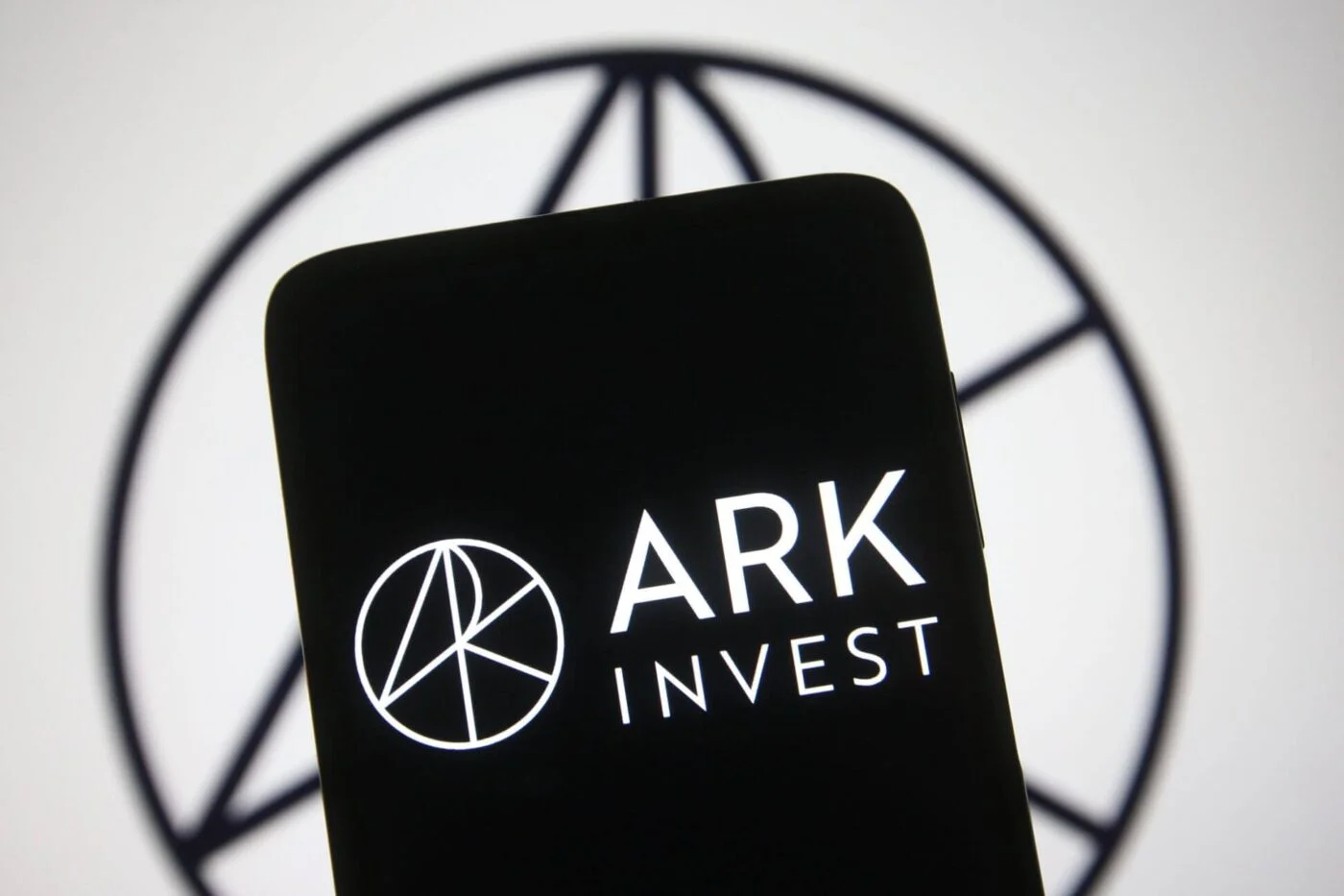 Логотип ARK Invest отображается на экране смартфона на размытом фоне с круглым гербом компании.