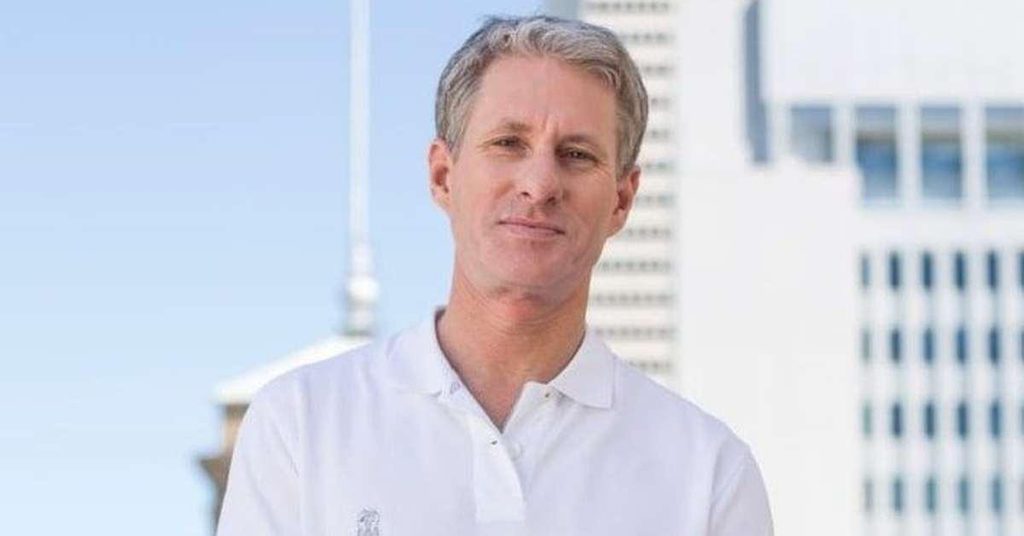 Image of Chris Larsen wearing a white shirt with a white skyscraper in the background