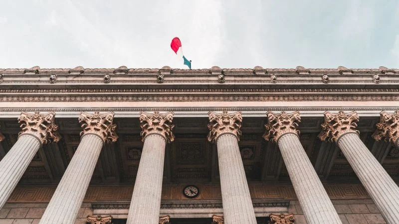 Low-angle view of a neoclassical government building with tall columns and the Italian flag flying above.